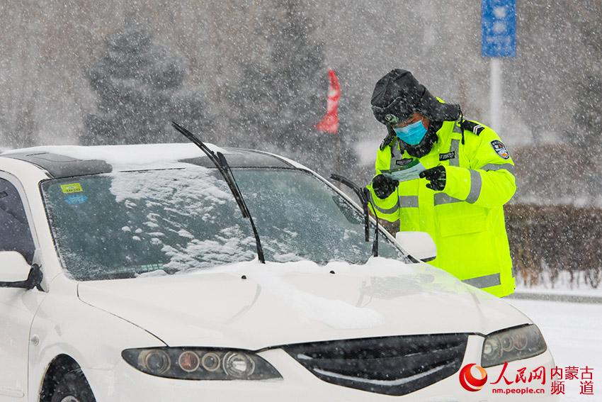 2月14日，阿魯科爾沁旗交通管理大隊民警在風雪中堅守防疫一線，維持交通秩序、進行道路清掃等工作，並對過往車輛及人員進行檢測、登記。張棖 張青林攝影報道