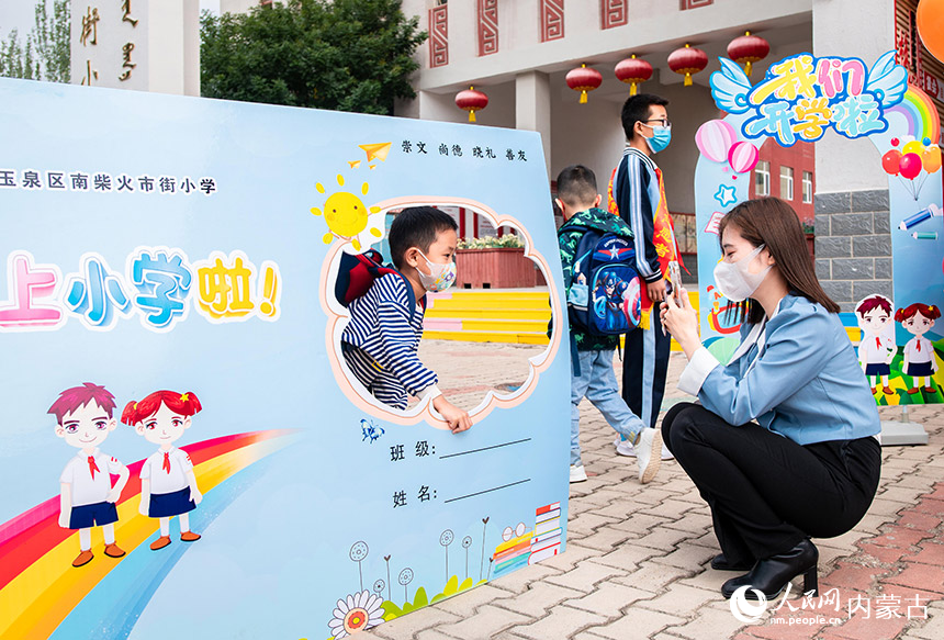呼和浩特市玉泉区南柴火市街小学一年级新生与“学生证”特色海报合影留念。丁根厚摄