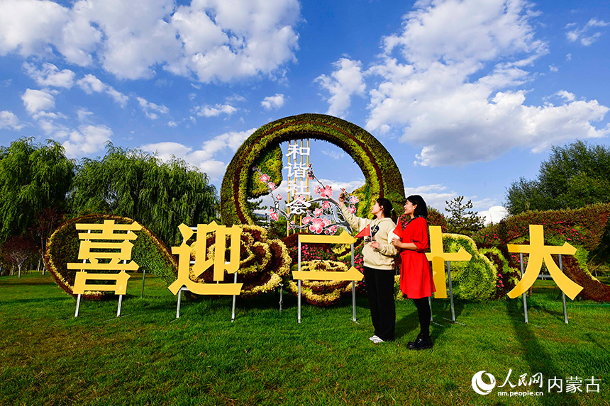 游客在鄂尔多斯市康巴什区“祝福祖国 喜迎二十大”主题花坛前拍照留念。王正摄