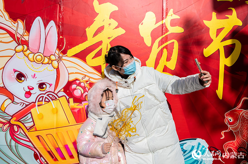 家长陪伴孩子在塞上老街年货节上选购糖画后拍照打卡。丁根厚摄