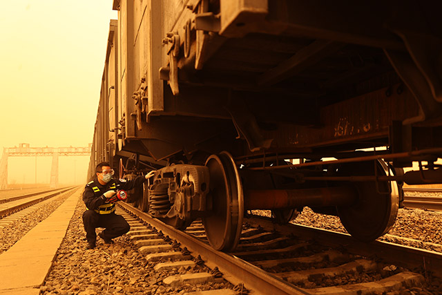 满洲里边检站民警在沙尘天气下对货运列车进行车体检查。安吉拉摄