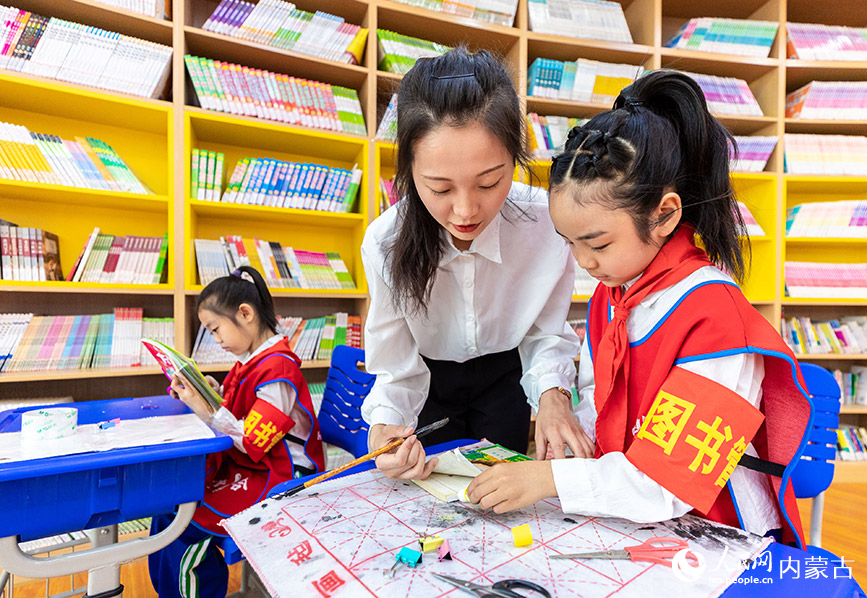4月19日，呼和浩特市玉泉区通顺街小学“小小图书管理员”和老师在“图书走廊”里修补破损图书。丁根厚摄