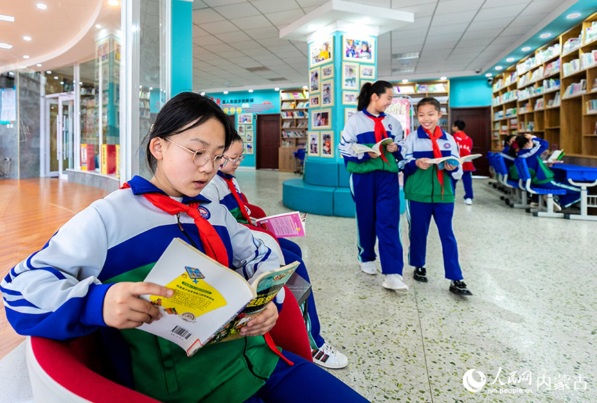 4月19日，呼和浩特市玉泉区通顺街小学学生利用课间休息时间在“图书走廊”翻阅图书。丁根厚摄