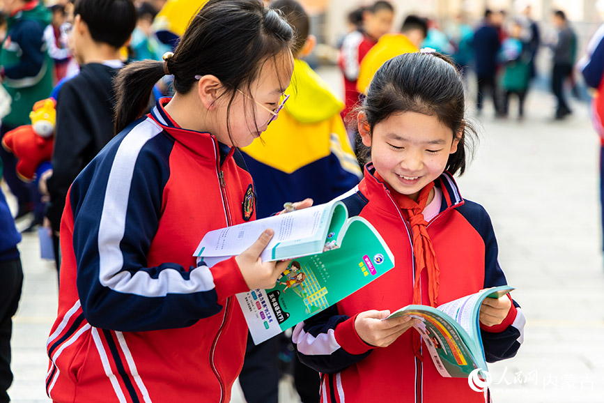 4月21日，呼和浩特市玉泉区恒昌店巷小学学生在“跳蚤市场”上翻阅购买的图书。丁根厚摄