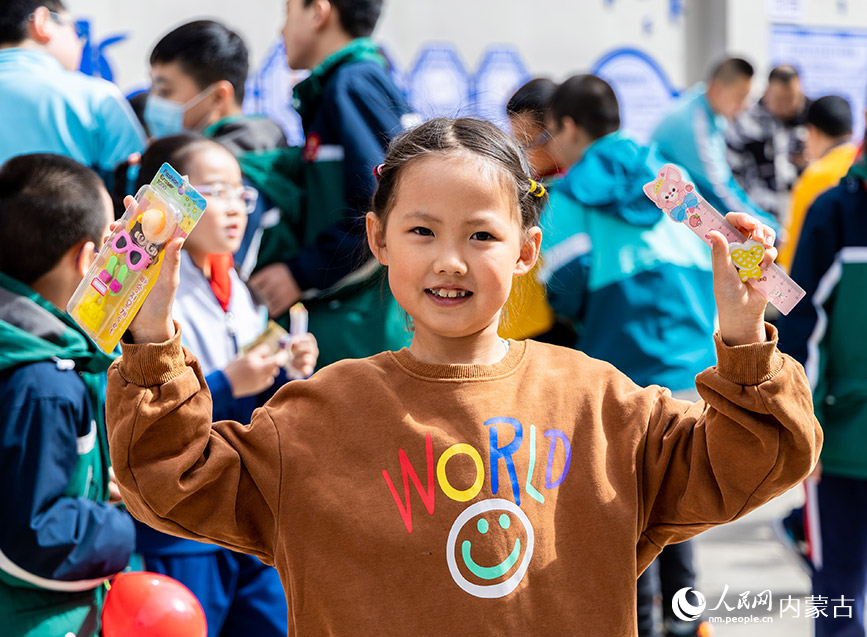 4月21日，呼和浩特市玉泉区恒昌店巷小学学生在“跳蚤市场”上向小伙伴展示交换来的文具。丁根厚摄