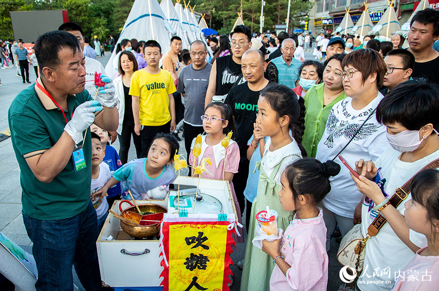 游客在呼和浩特市玉泉区大召历史文化广场观看非遗传承人表演吹糖人。丁根厚摄