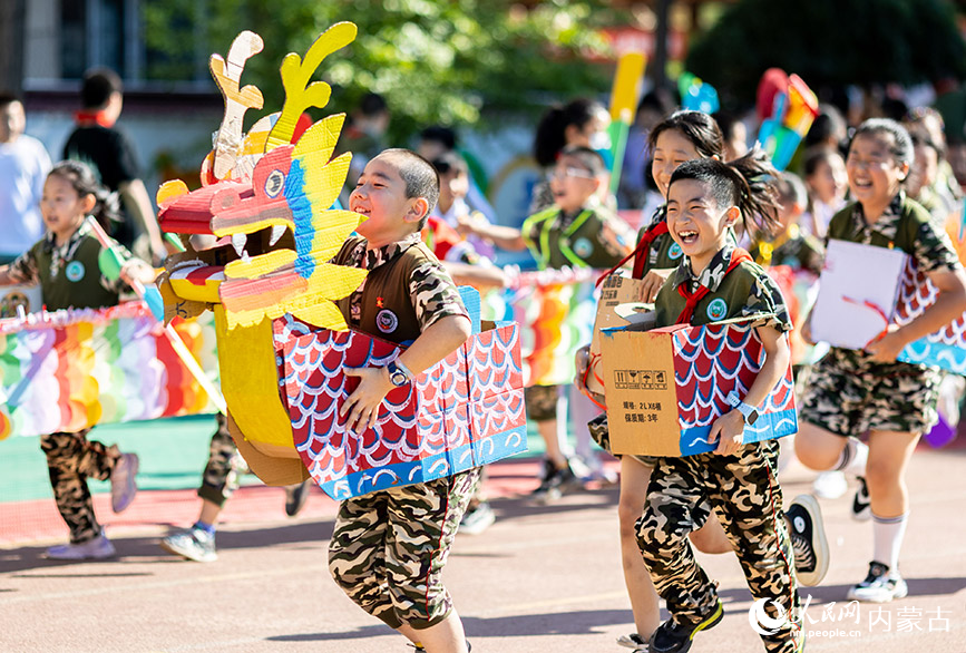 6月20日，内蒙古呼和浩特市玉泉区五塔寺东街小学学生在进行“旱地龙舟”趣味比赛。丁根厚摄