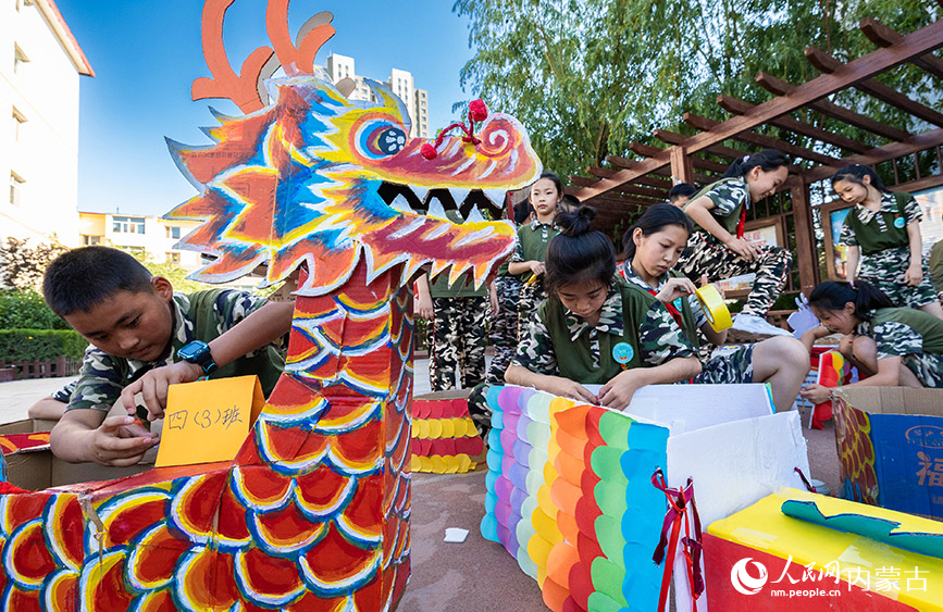 6月20日，内蒙古呼和浩特市玉泉区五塔寺东街小学学生在校园内组装准备参赛的“龙舟”。丁根厚摄
