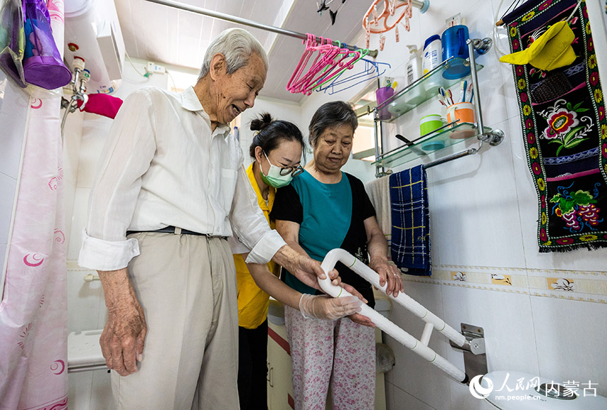 护理员在呼和浩特市玉泉区康乐社区87岁的低保户老人吕金福家中演示卫生间U型助力扶手的使用方法。丁根厚摄