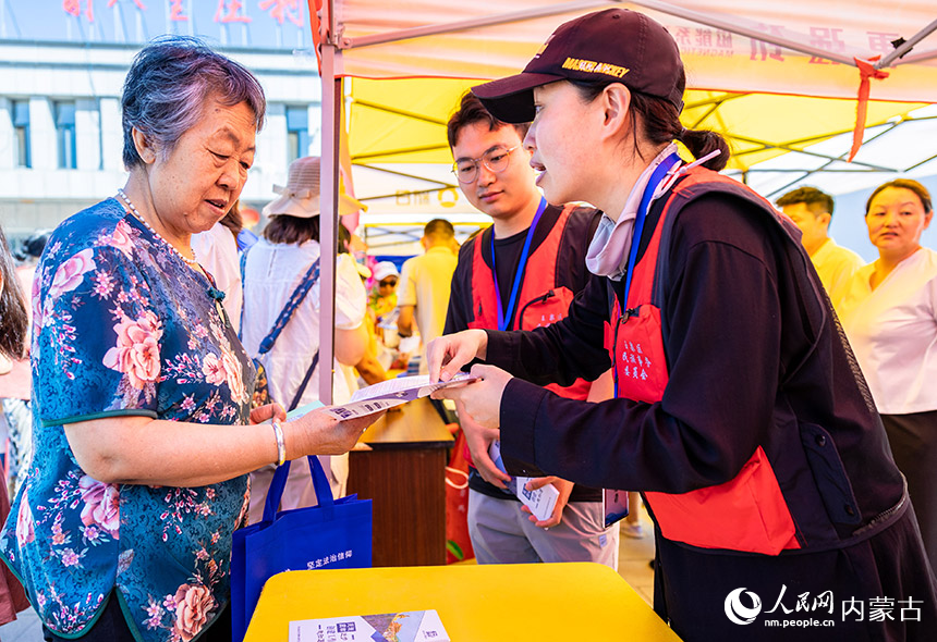玉泉区民委的志愿者在呼和浩特市玉泉区前八里庄村鲜食玉米丰收节上为村民发放宣传材料。丁根厚摄
