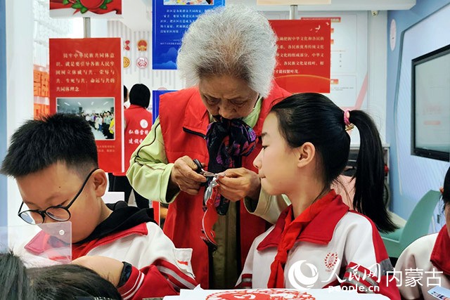 “银龄红”党支部党员志愿者于丰成正在教小朋友剪纸。实习生 王泽桐摄