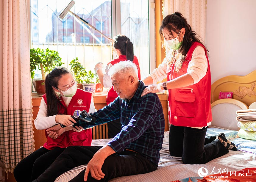 呼和浩特市玉泉区民政局的党员志愿者上门为社区老人李国材提供保健按摩服务。丁根厚摄