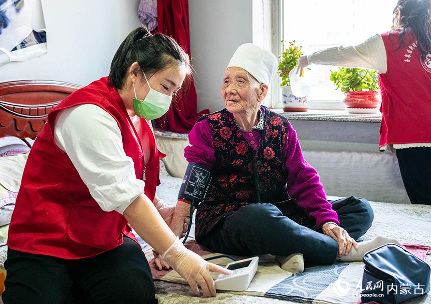 呼和浩特市玉泉區民政局的黨員志願者上門為社區老人呂桂雲提供測量血壓等服務。丁根厚攝