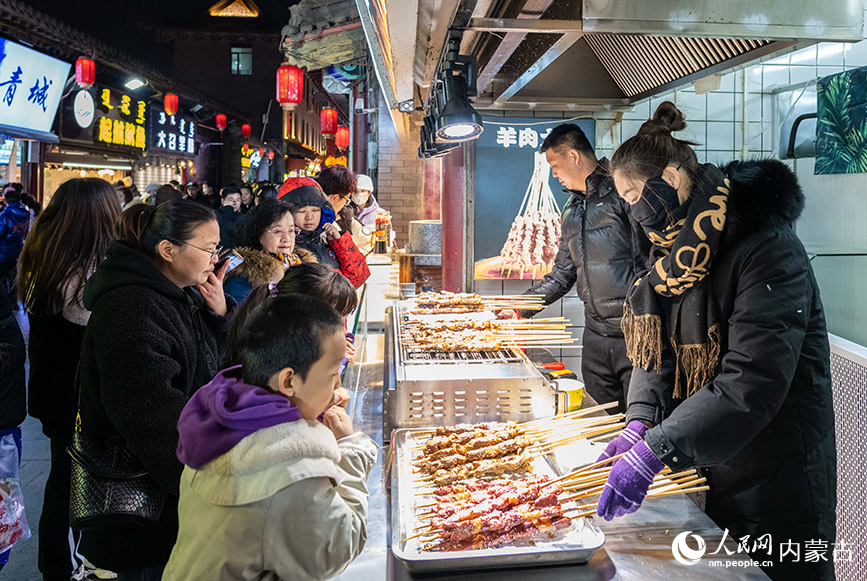2023年12月31日，游人在呼和浩特市玉泉区塞上老街旅游休闲街区跨年夜活动现场选购特色小吃。丁根厚摄