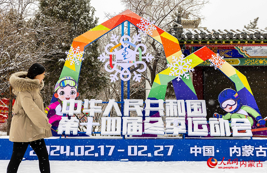 2024年1月19日，游人冒雪从呼和浩特市玉泉区塞上老街旅游休闲街区设置的“十四冬”宣传造型旁经过。丁根厚摄