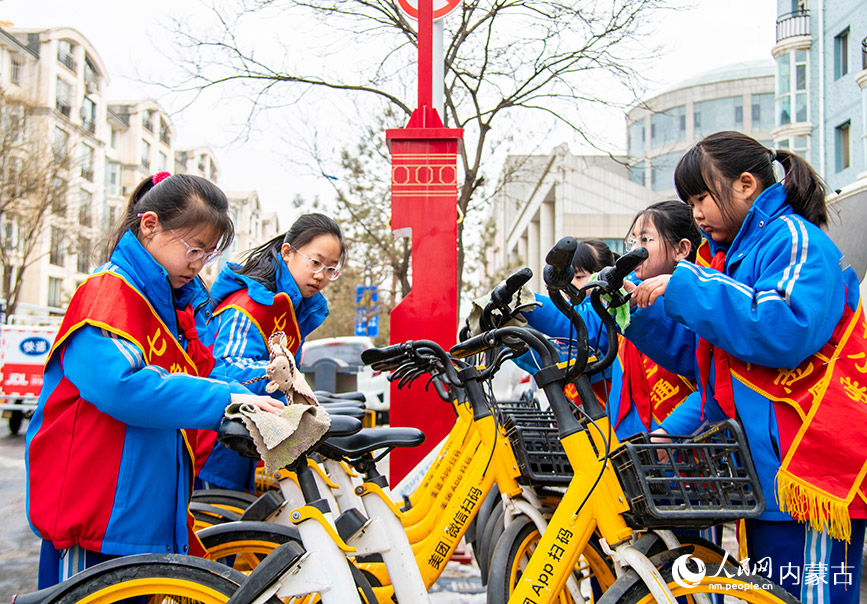 3月4日，呼和浩特市玉泉区通顺街小学学生在街头清洁公共自行车。丁根厚摄