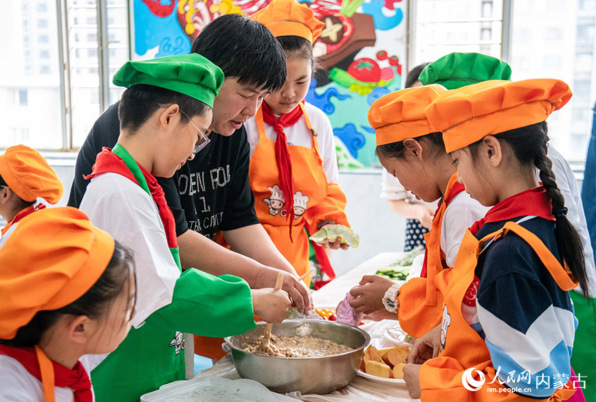 5月24日，呼和浩特市玉泉区南柴火市街小学学生在“烹饪课堂”上学习搅拌烧麦馅。丁根厚摄