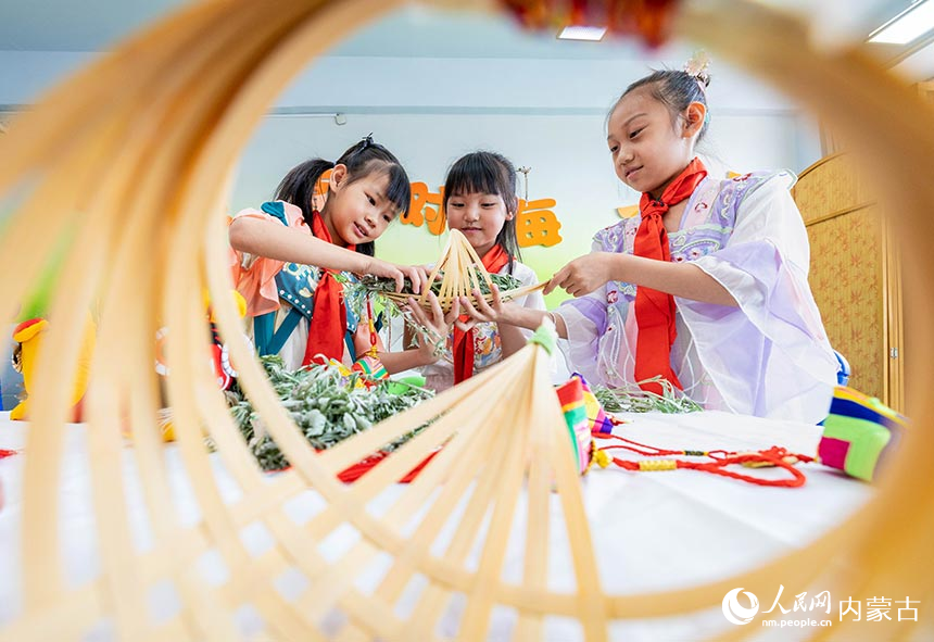 呼和浩特市玉泉区通顺街小学学生在“我们的节日·端午”主题活动上将艾草装进竹船。丁根厚摄