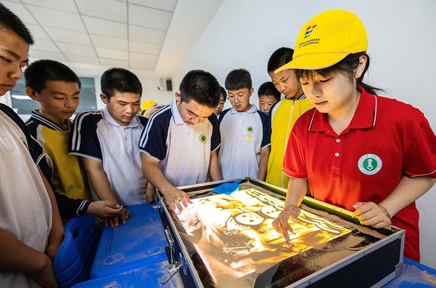 大学生志愿者在呼和浩特市第十二中学乡村少年宫指导学员们练习沙画。丁根厚摄