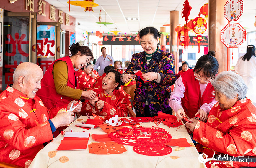 1月20日，志愿者与老人们在呼和浩特市玉泉区民政局迎新春主题活动现场一起剪窗花。丁根厚摄