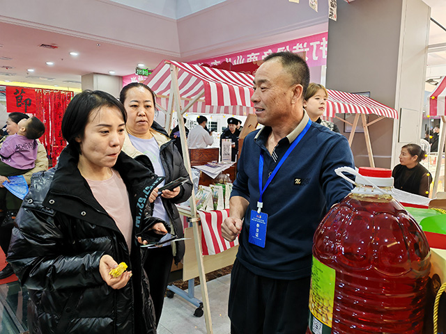 年货节现场，摊主向顾客介绍商品，氛围热闹。郑明摄