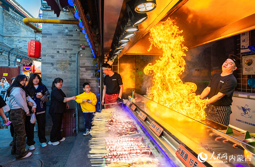 5月1日，摊主在第六届塞上老街音乐美食季夜市街区为游客制作火爆鱿鱼。丁根厚摄