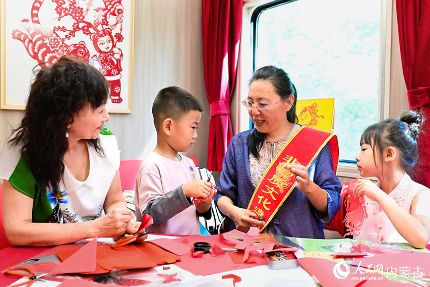 8月10日,非遺傳承人張燁楠(右二)在“阿爾山號”旅游專列上向游客傳授剪紙技藝。王正攝