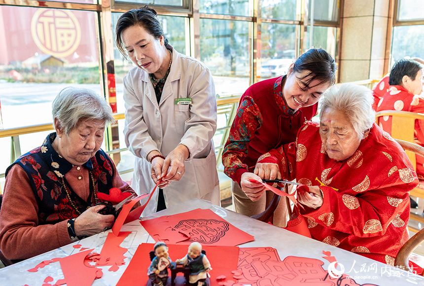 护理员陪伴老人们在呼和浩特市玉泉区民政局“爱心敬老 情暖重阳”主题活动现场一起剪纸。丁根厚摄