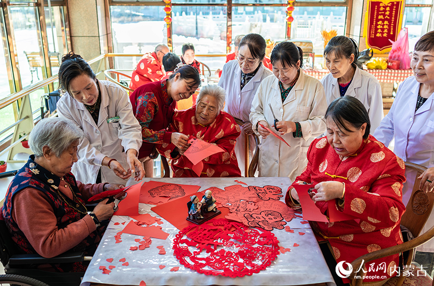 护理员陪伴老人们在呼和浩特市玉泉区民政局“爱心敬老 情暖重阳”主题活动现场一起剪纸。丁根厚摄