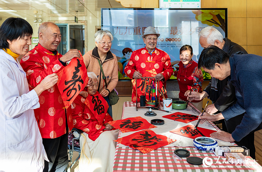文化志愿者在呼和浩特市玉泉区民政局“爱心敬老 情暖重阳”主题活动现场为老人们书写“寿”字书法作品。丁根厚摄