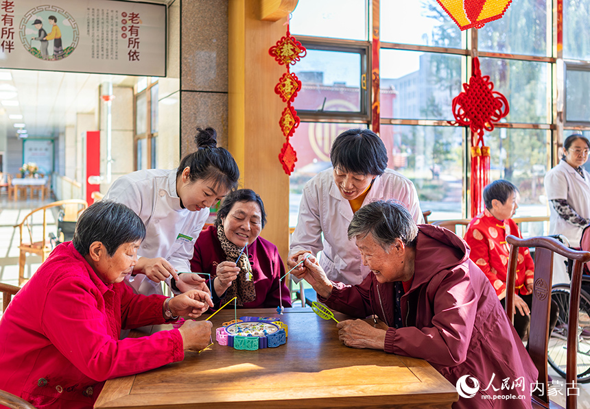 护理员陪伴老人们在呼和浩特市玉泉区民政局“爱心敬老 情暖重阳”主题活动现场玩益智游戏。丁根厚摄