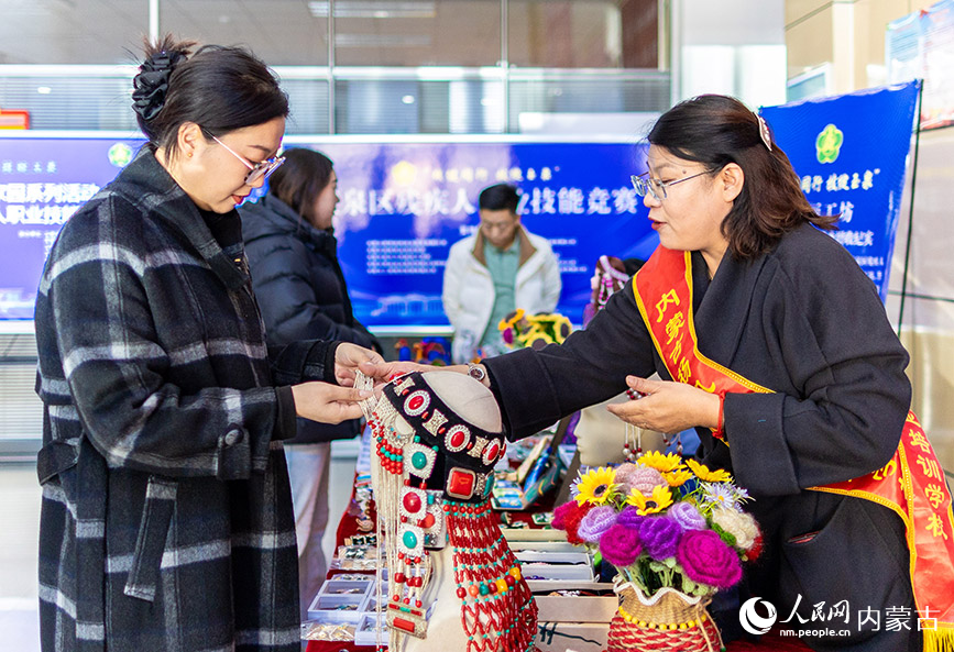 11月16日，呼和浩特市玉泉区残疾人职业技能竞赛现场，市民在残疾人就业成果展示区了解一款“敕勒川巧娘”手工艺品。丁根厚摄
