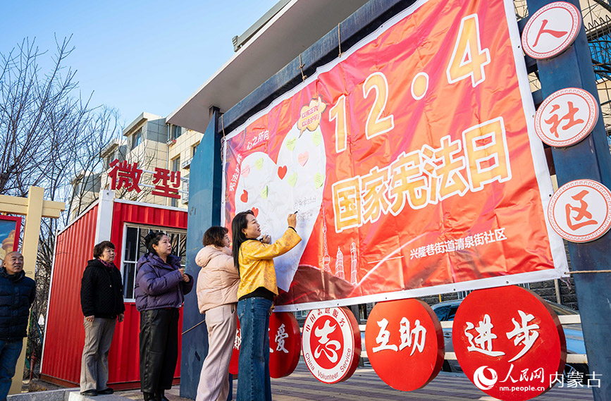 12月4日，呼和浩特市玉泉区清泉街社区居民在“国家宪法日”主题宣传展板上签名。丁根厚摄