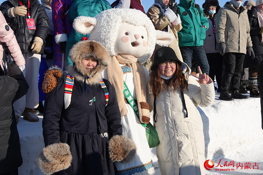 游客和冰雪那达慕吉祥物“呼伦小羊”合影。人民网记者 赵梦月摄