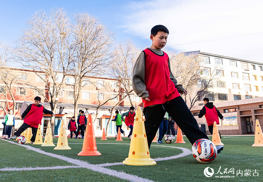 2月1日，呼和浩特市玉泉区南茶坊小学校园足球冬训活动现场，小球员们在绿茵场上练习运球。丁根厚摄