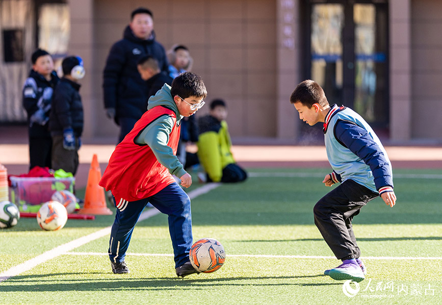 2月1日，呼和浩特市玉泉区南茶坊小学校园足球冬训活动现场，小球员们在绿茵场上进行足球分组对抗赛。丁根厚摄