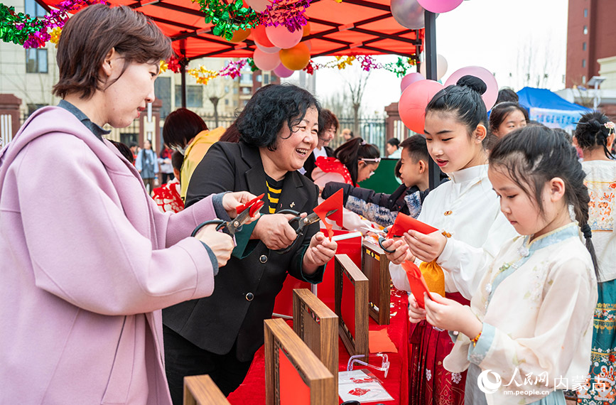 3月27日，呼和浩特市新城区北垣小学新雅校区第四届校园风筝节活动现场，学生在体验剪纸技艺。丁根厚摄