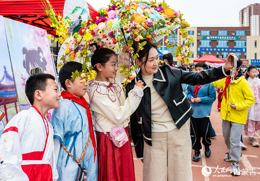 3月27日，呼和浩特市新城区北垣小学新雅校区第四届校园风筝节活动现场，学生们手持花伞与家长打卡拍照。丁根厚摄