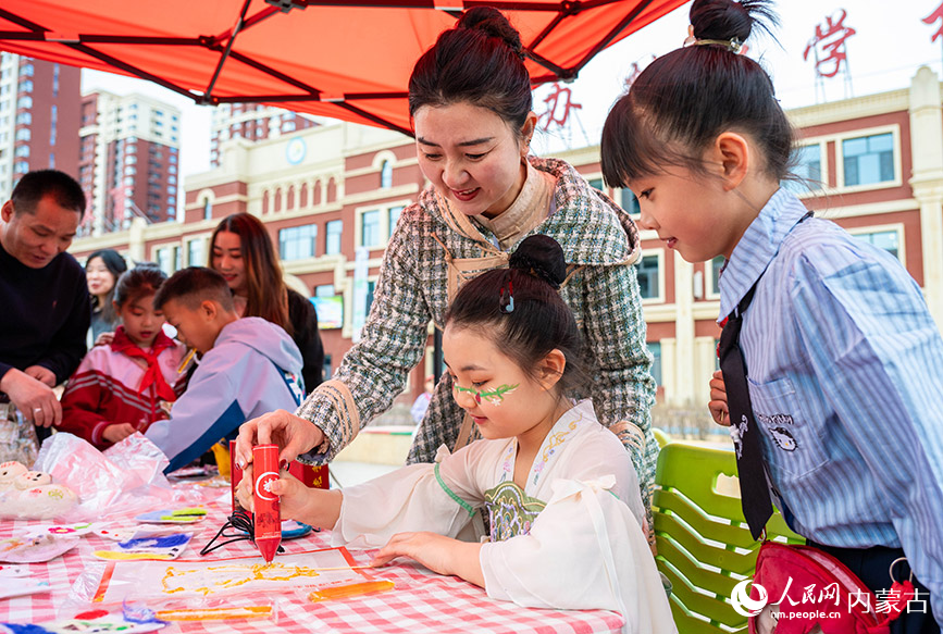 3月27日，呼和浩特市新城区北垣小学新雅校区第四届校园风筝节活动现场，学生与家长在共同制作糖画。丁根厚摄