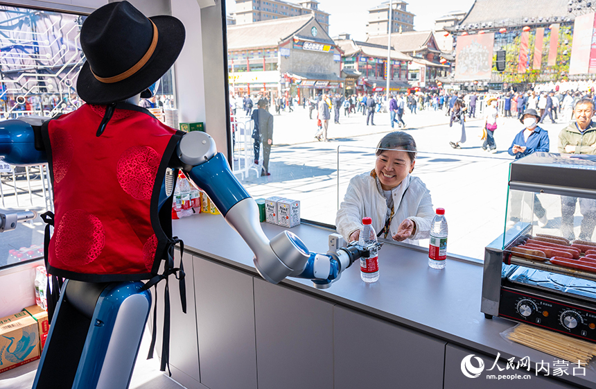 玉泉区塞上老街旅游休闲街区，人形机器人在智能零售舱内为游客递送饮品。丁根厚摄