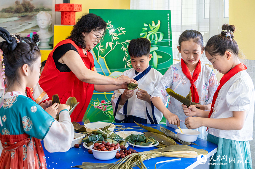 呼和浩特市玉泉区五塔寺东街小学“我们的节日·端午”主题活动现场，志愿者教学生们包粽子。丁根厚摄