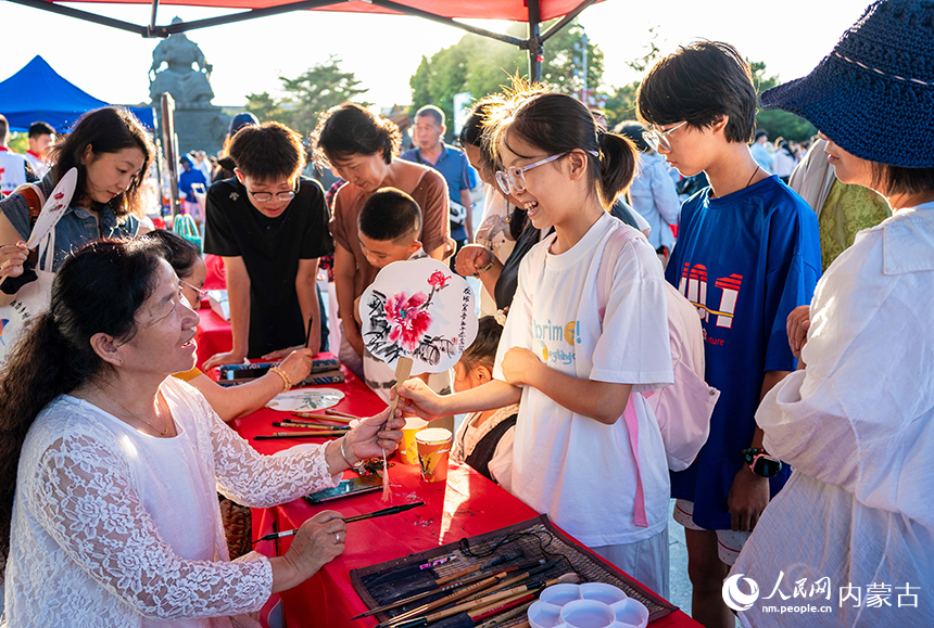 呼和浩特市玉泉区“文明市集”活动现场，文化志愿者为市民绘制赠送彩扇。丁根厚摄
