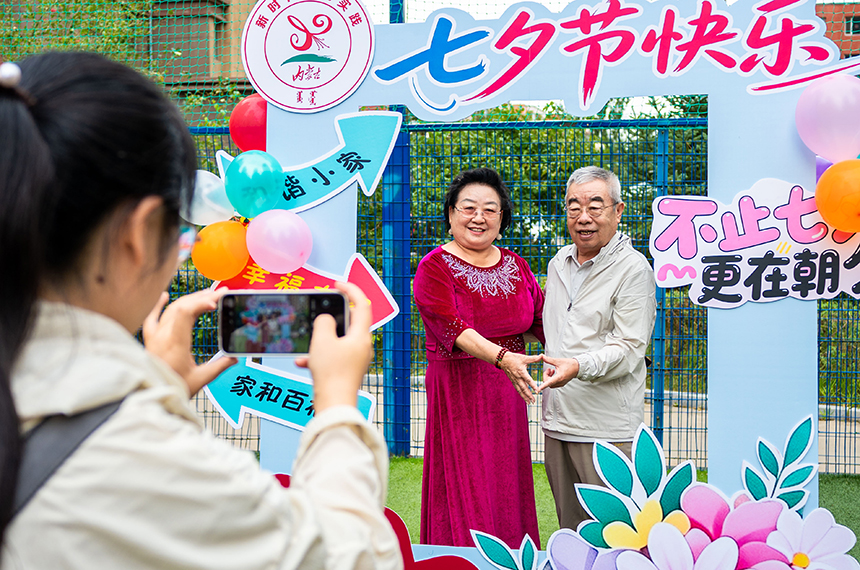 呼和浩特市玉泉區“愛在‘七夕’踐文明 和諧家風共傳承”主題文明市集活動現場，志願者在為老年夫妻拍攝“七夕”紀念合影。丁根厚攝