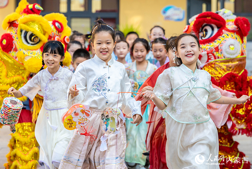 呼和浩特市玉泉区清泉街小学“品民俗 迎中秋”主题活动现场，学生们手持花灯与舞狮互动欢呼。丁根厚摄